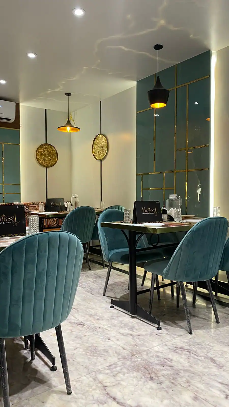 Viraasat restaurant interior — warm beige walls, gold accents, and forest-green seats